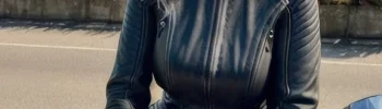 A smiling, middle-aged woman dressed in a black leather outfit, sitting on a motorbike.