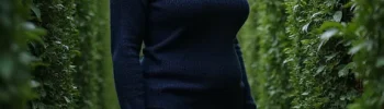 A woman standing in a maze with high hedge walls on all sides.